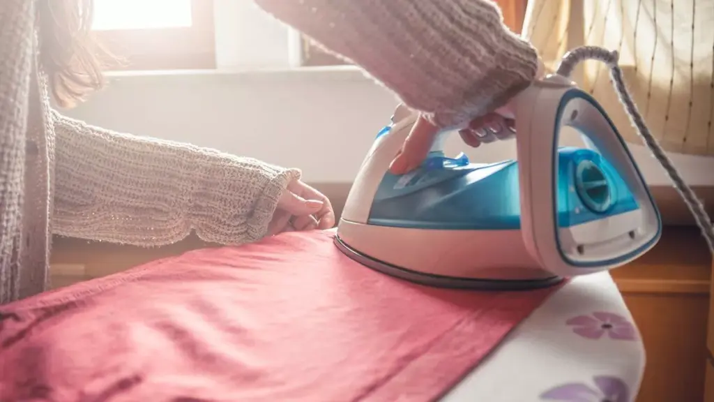 Pessoa utilizando ferro de passar roupa em tábua